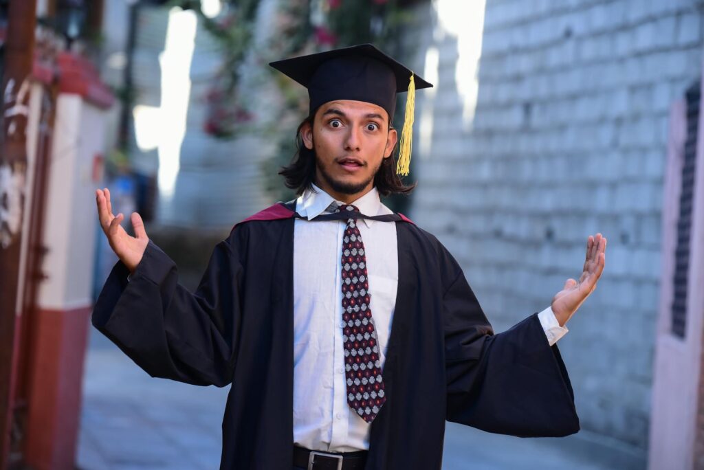 A happy graduate student wearing a black cap and gown holds a diploma and smiles at the camera.