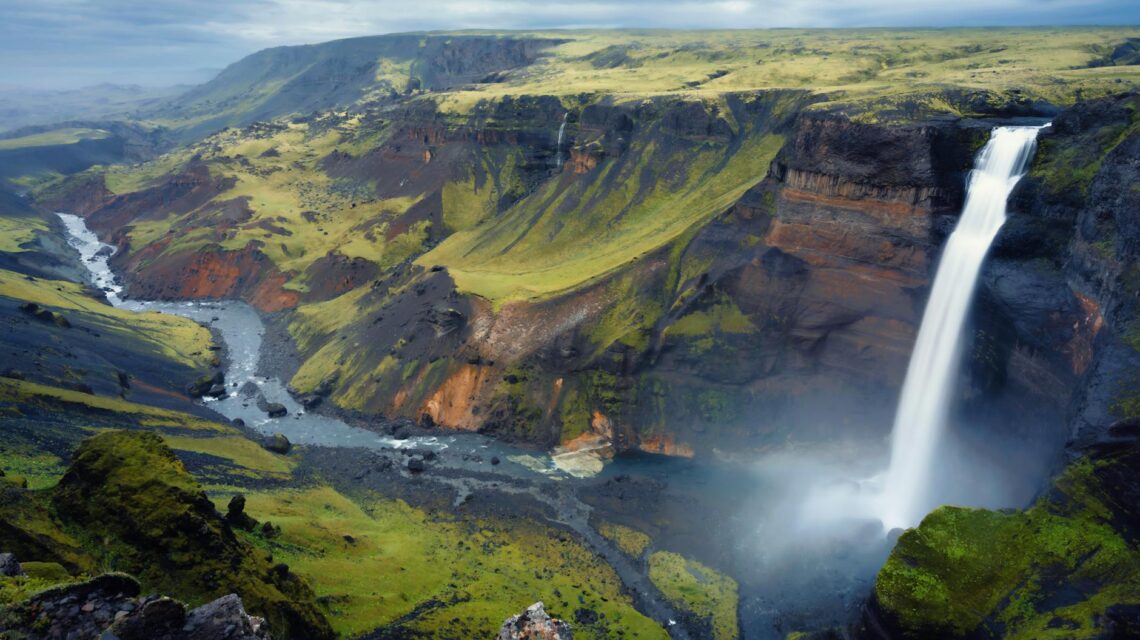 The iconic Múlafossur waterfall cascading over a dramatic cliff into the Atlantic Ocean in the Faroe Islands.