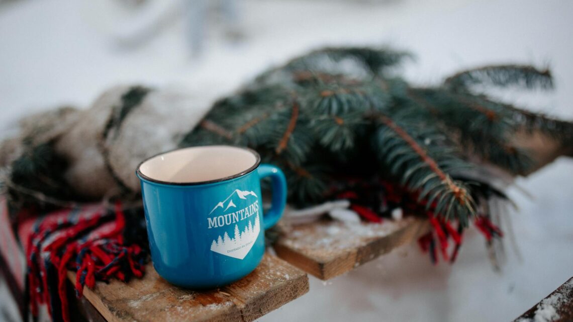 A person's feet in cozy socks propped up near a warm fireplace, with a steaming mug of tea on a small table.