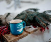 A person's feet in cozy socks propped up near a warm fireplace, with a steaming mug of tea on a small table.