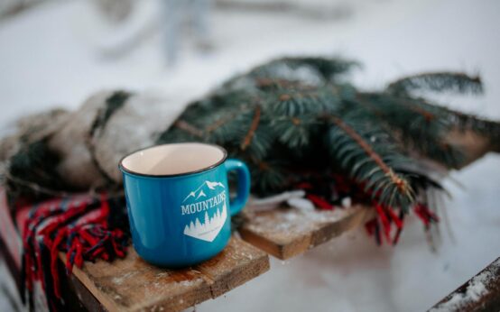 A person's feet in cozy socks propped up near a warm fireplace, with a steaming mug of tea on a small table.