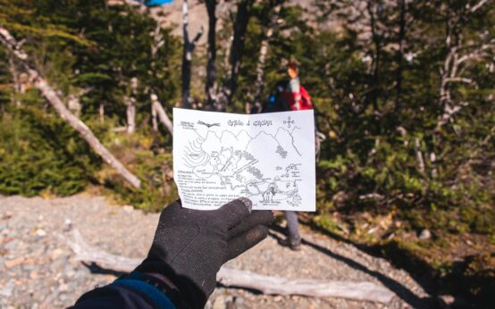 A traveler in hiking gear consults a foldable paper map while standing on a forest trail.