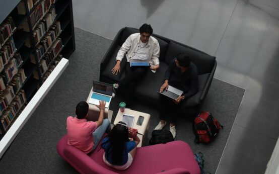 A diverse group of university students sitting at a table, focused on their work on various laptops.