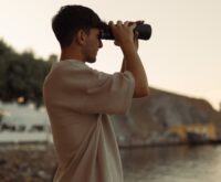 A traveler standing on a scenic overlook, using binoculars to watch birds in the distance.
