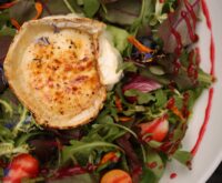 A white ceramic bowl filled with a colorful mix of blueberries, strawberries, and spinach.