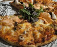 A beautifully plated grilled salmon fillet sits next to a colorful assortment of roasted asparagus, cherry tomatoes, and lemon slices.