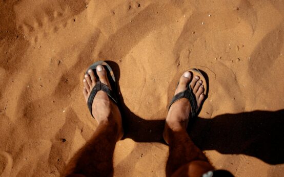 A person's feet propped up on a poolside lounge chair next to a colorful cocktail.