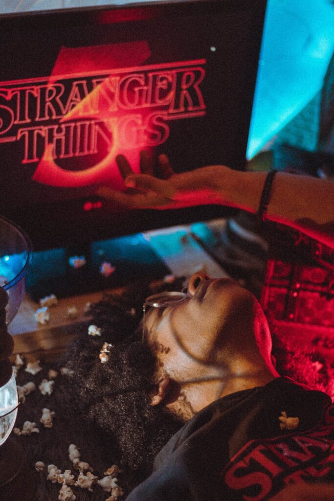 A person's feet are visible as they relax in a hammock, with a canopy of green leaves and a blue, cloud-strewn sky above.