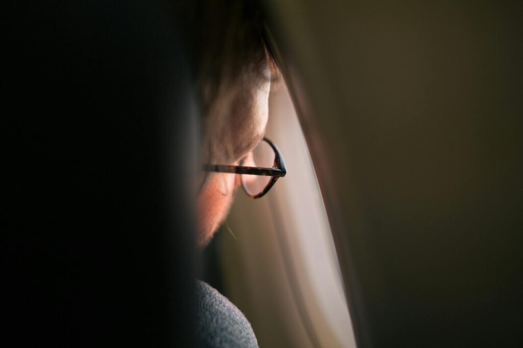 A pensive male student wearing noise-canceling headphones gazes out of a rain-streaked window, taking a break from studying.