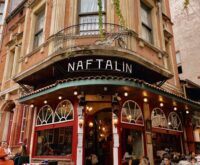 A person wearing headphones stands on a balcony, thoughtfully observing the busy city life below.