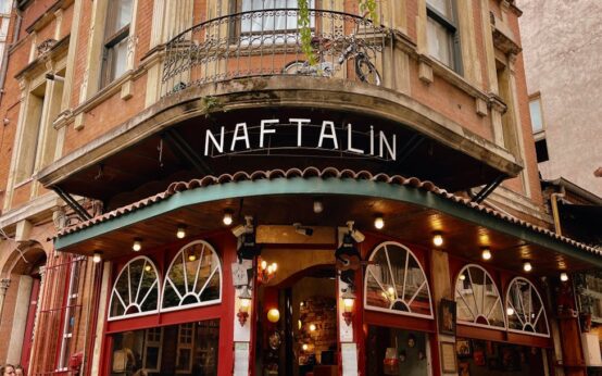 A person wearing headphones stands on a balcony, thoughtfully observing the busy city life below.