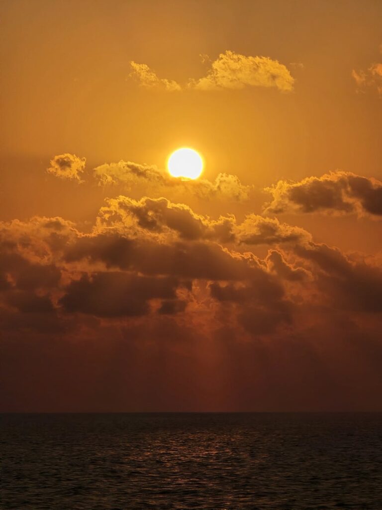 Vibrant orange and purple stratocumulus clouds paint the sky during a dramatic sunset over a calm sea.