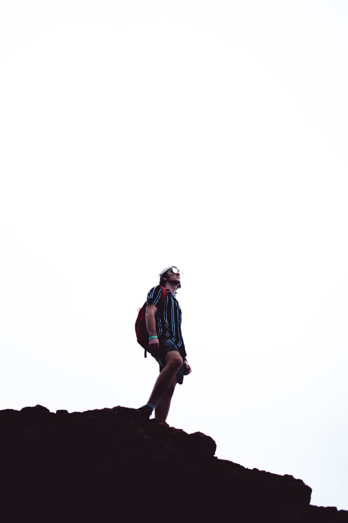 A female hiker with a backpack standing on a cliff, overlooking a vast mountain range at sunrise.