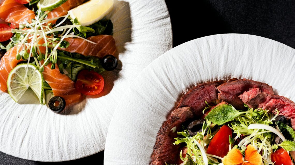 A perfectly grilled salmon fillet sits on a bed of dark leafy greens, adorned with a bright yellow lemon wedge.