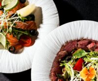 A perfectly grilled salmon fillet sits on a bed of dark leafy greens, adorned with a bright yellow lemon wedge.