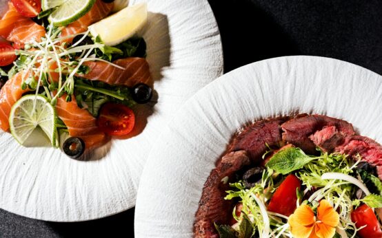 A perfectly grilled salmon fillet sits on a bed of dark leafy greens, adorned with a bright yellow lemon wedge.