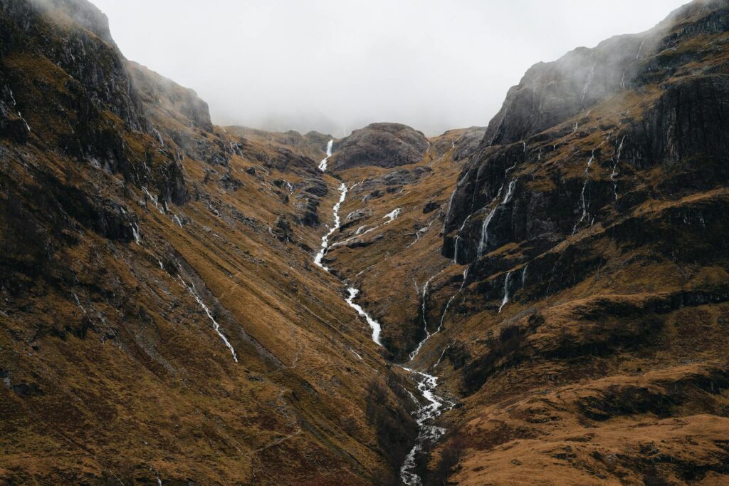 A tranquil Scottish loch with low-hanging mist obscuring the mountains in the background.