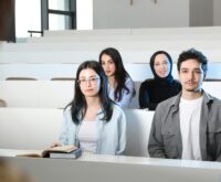 A diverse group of university students sitting at a table with books and laptops, engaged in a study session.
