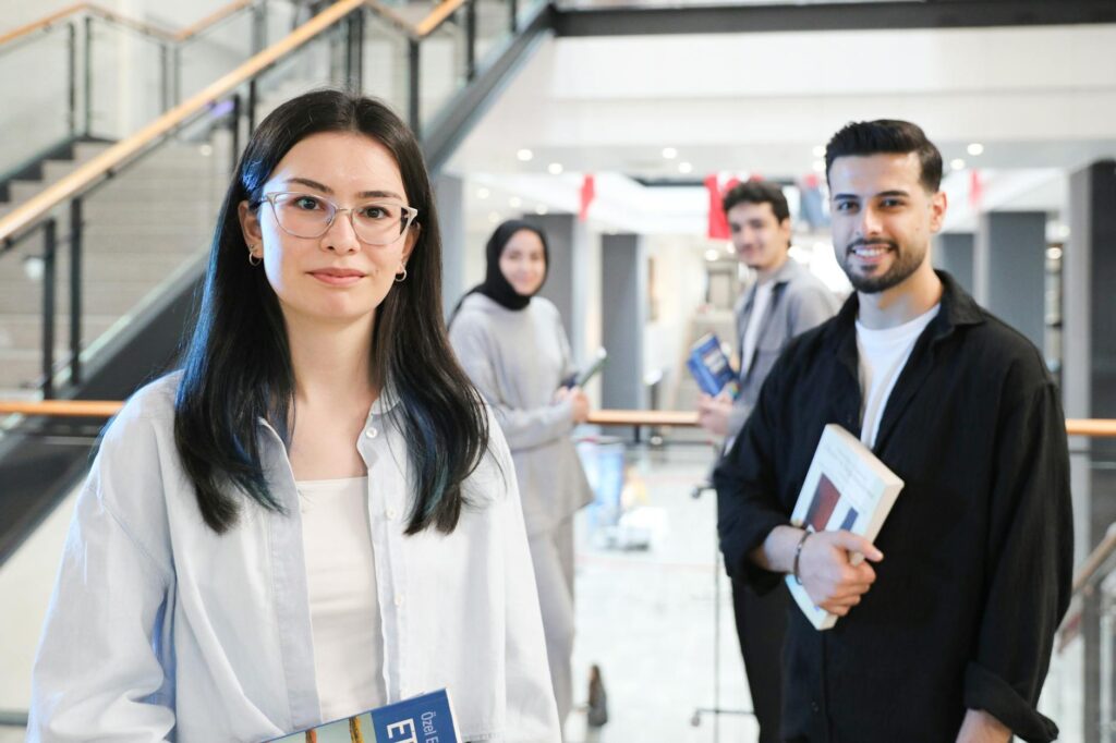 Four college students of different ethnicities smiling and working together around a table with a laptop.