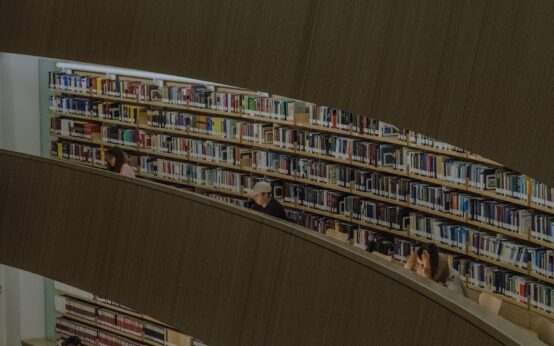 A diverse group of university students studying together around a large table in a sunlit, modern library.