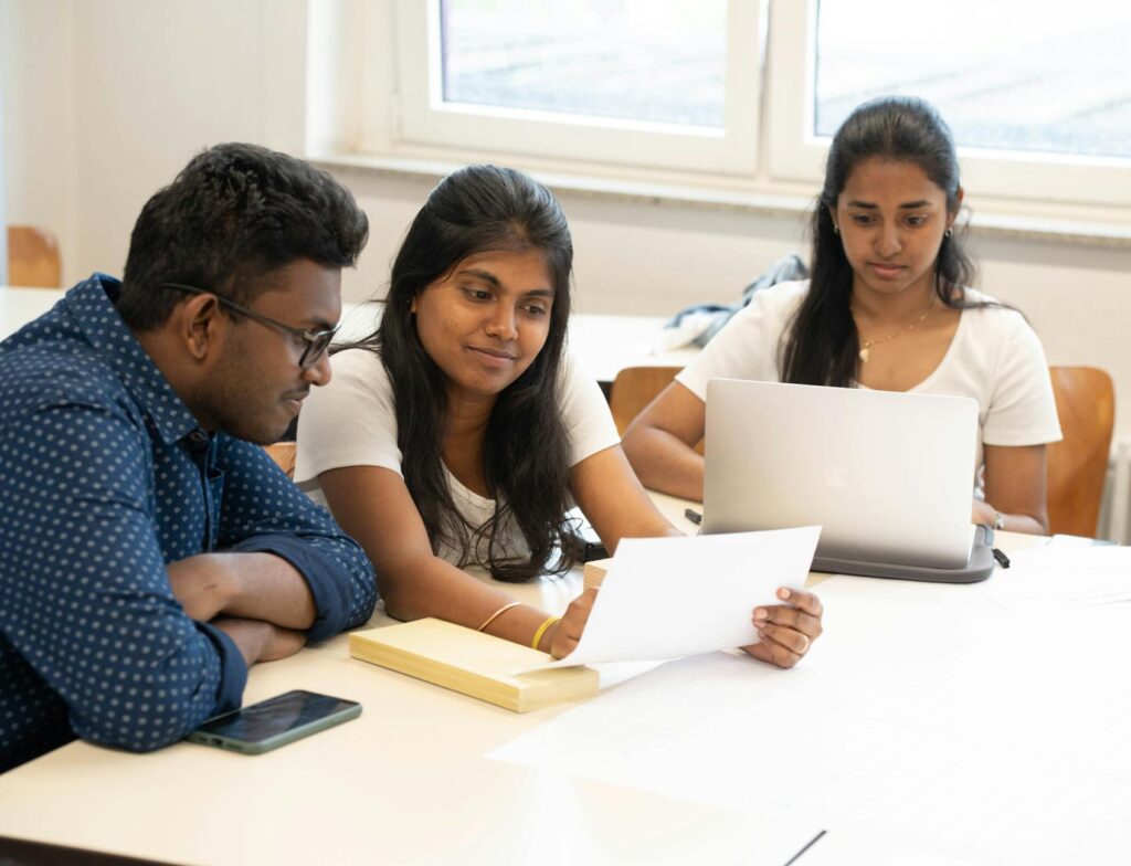 A diverse group of four college students laughing and pointing at a laptop screen while working together.