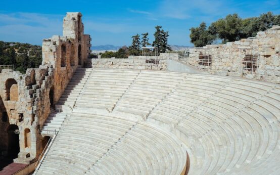 The sun-bleached stone tiers of an empty ancient Greek amphitheater, overlooking a serene landscape.