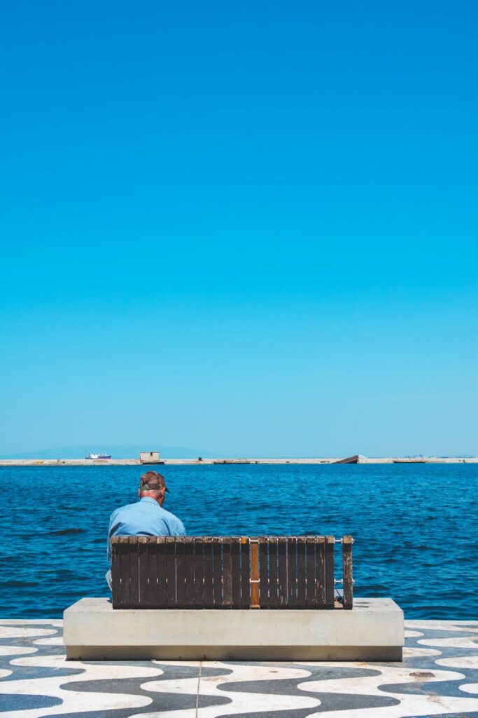 A single person sits on a bench in a modern, deserted airport terminal, with long shadows stretching across the polished floor.