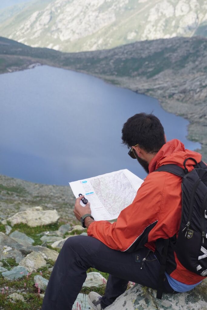 A hiker consults a paper topographical map while resting on a trail in the mountains.