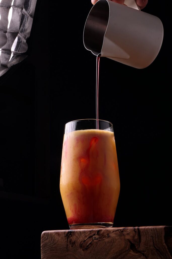 A person's bare feet resting on a sunlit wooden deck next to a tall glass of orange juice.