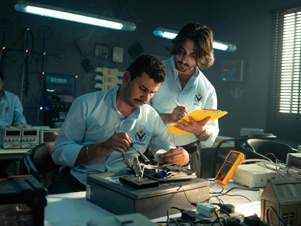 Three focused students in lab coats looking intently at a test tube in a modern science laboratory.