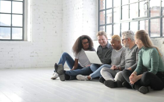 A diverse group of students in a modern classroom, working together on a laptop, showcasing collaboration and technology.