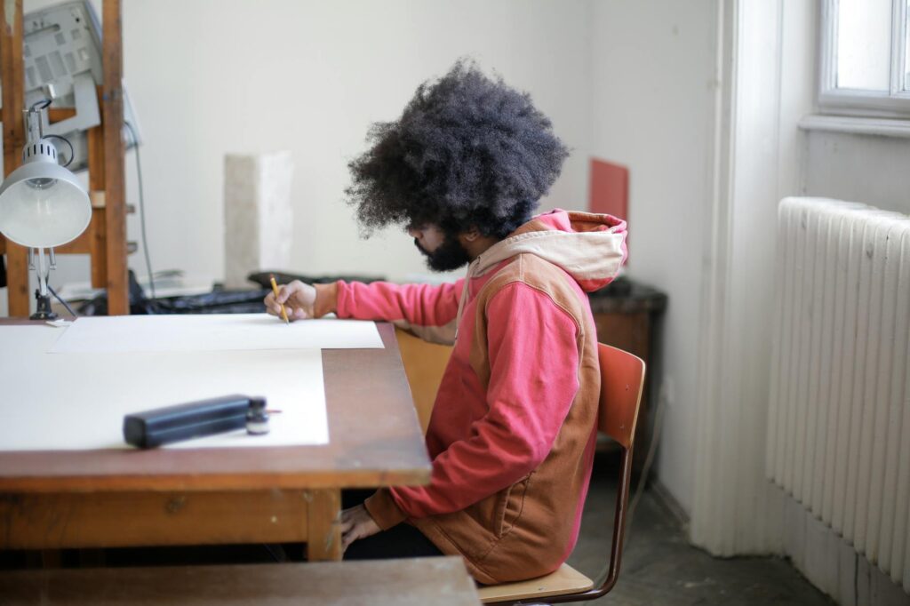 An art student with a pencil in hand concentrates on a detailed sketch in a sunlit art studio.