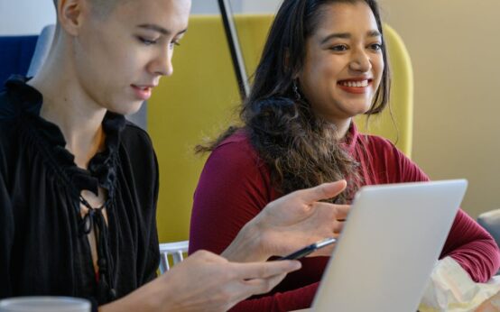 A diverse group of university students collaborating around a laptop in a bright, modern library.