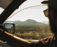 A traveler gazes out the window of a train at a passing green and mountainous landscape.