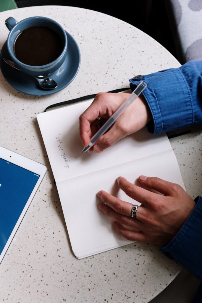 Close-up of a student's hands writing detailed notes in a spiral notebook, with morning light streaming in.