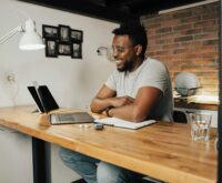 A university student sitting at a desk with a laptop, tutoring online from their dorm room.