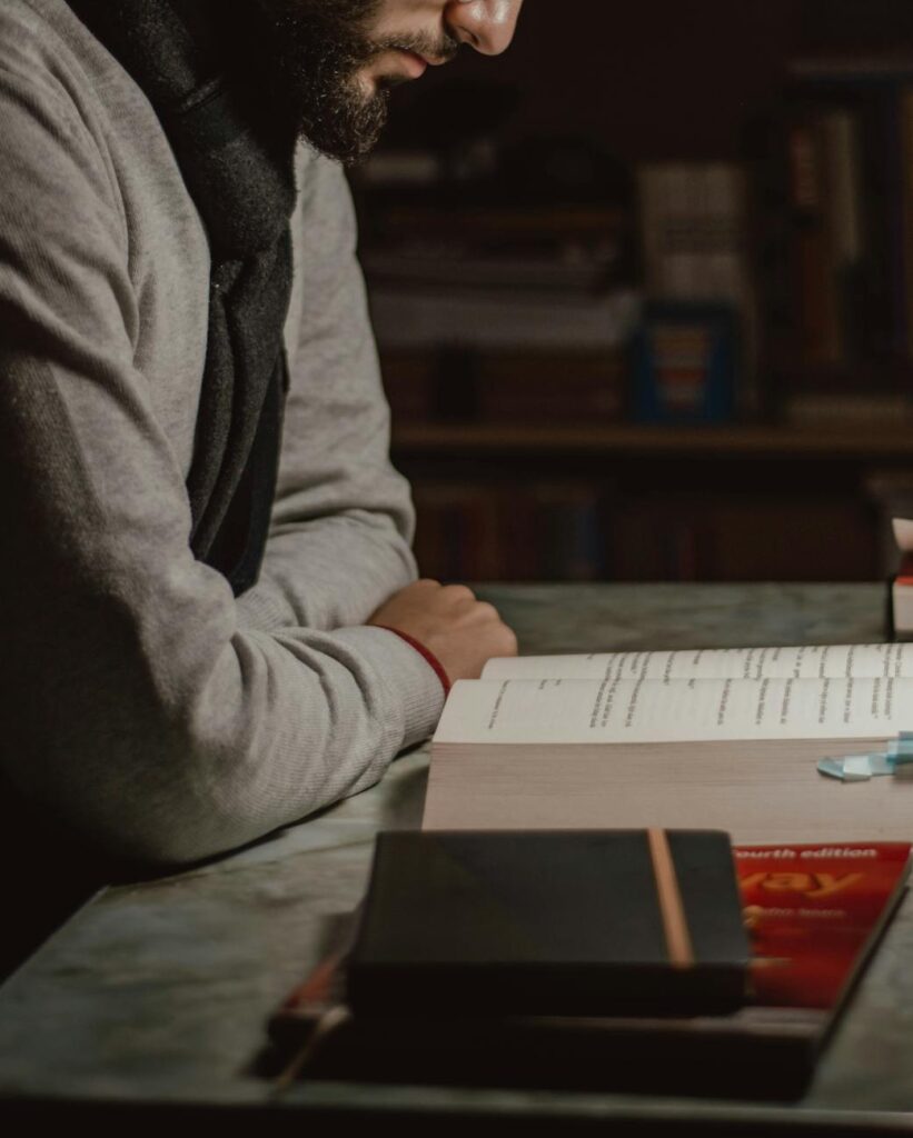 A focused student wearing headphones studies under a lamp in a quiet library, surrounded by stacks of books.