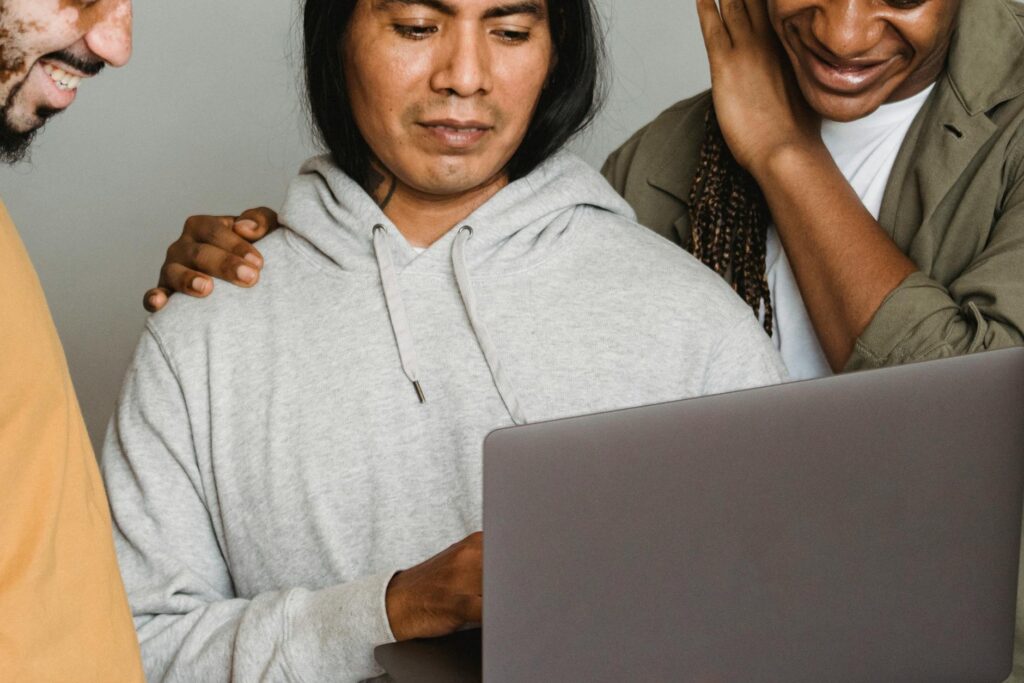 A diverse group of four students huddle around a laptop, showing signs of stress and disagreement.