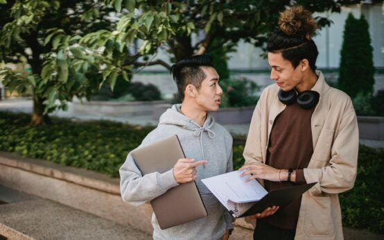 A diverse group of four university students smiling as they work together around a wooden table.