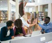 A diverse group of engineering students working together on a complex model in a university workshop.