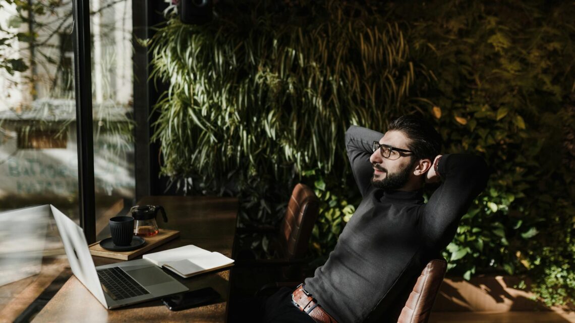 A business owner smiling while working on a laptop on a sunny beach, representing founder freedom.