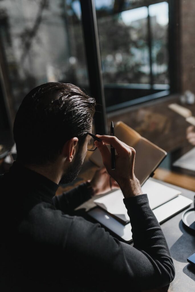 A person's hands writing in a travel journal, with a passport and a cup of tea visible on the table.