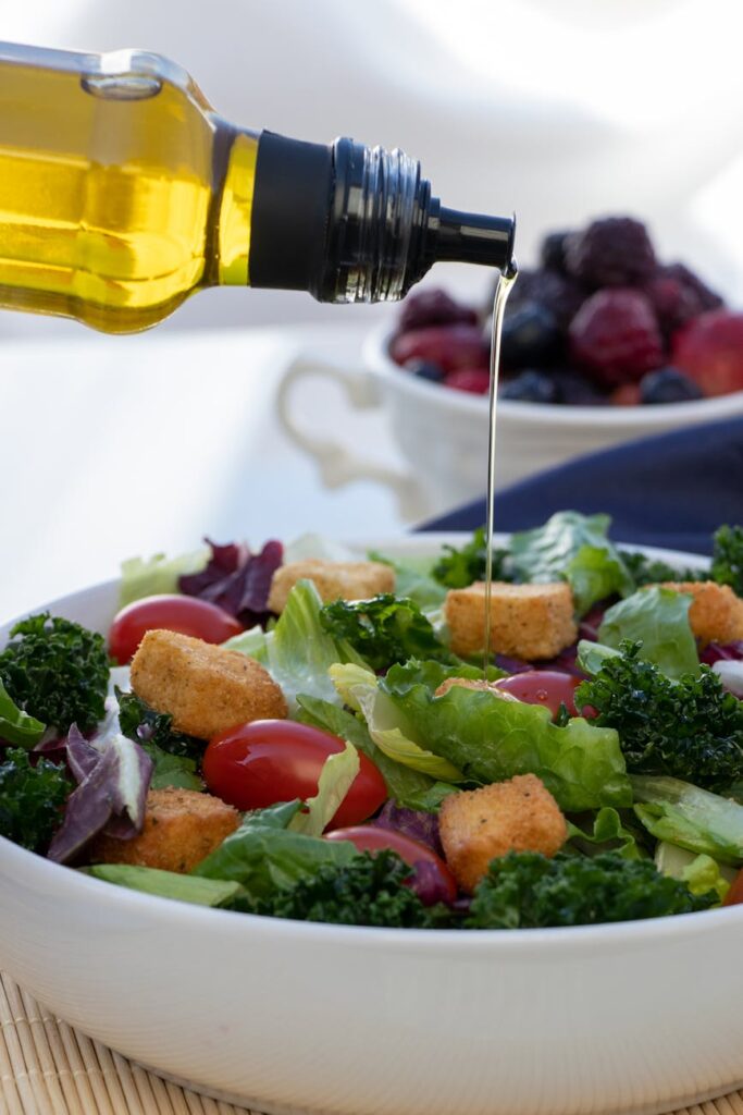 A close-up of hands drizzling extra virgin olive oil over a fresh Greek salad.