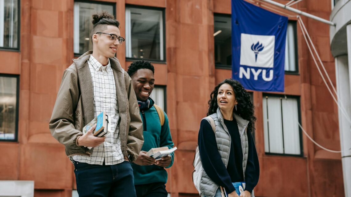 A diverse group of smiling university students gathered around a table with books and laptops.