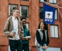A diverse group of smiling university students gathered around a table with books and laptops.