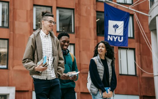 A diverse group of smiling university students gathered around a table with books and laptops.