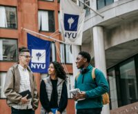 A diverse group of four university students smiling while studying around a wooden table in a sunlit room.