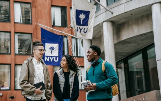 A diverse group of four university students smiling while studying around a wooden table in a sunlit room.