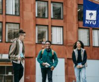A diverse group of college students smiling and studying together around a wooden table.