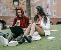 A diverse group of male and female university students working together around a table with laptops and notebooks.